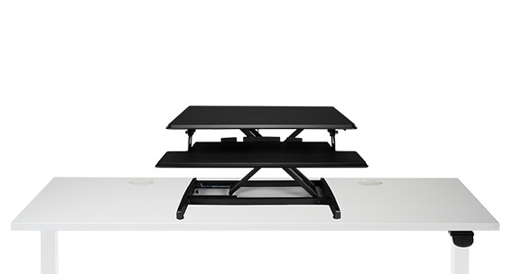 Black UPLIFT Lady Bird UDA124-BLK riser with an upper platform and lower keyboard shelf placed on a white host desk.