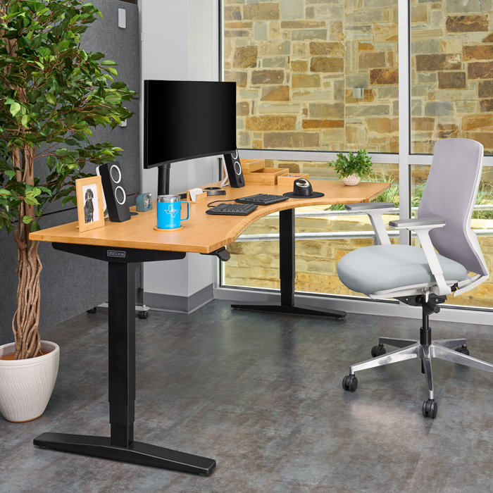 UPLIFT UPL969 curved-corner standing desk with a bamboo-colored top and black two-leg frame in a manufacturer environment image; the depicted keypad and grommet state is not confirmed.