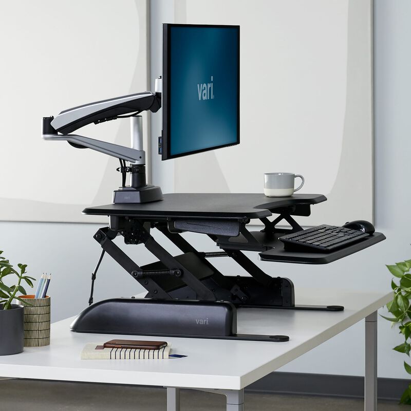 VariDesk Essential 30 black converter raised on a separate desk with monitor arm shown for context