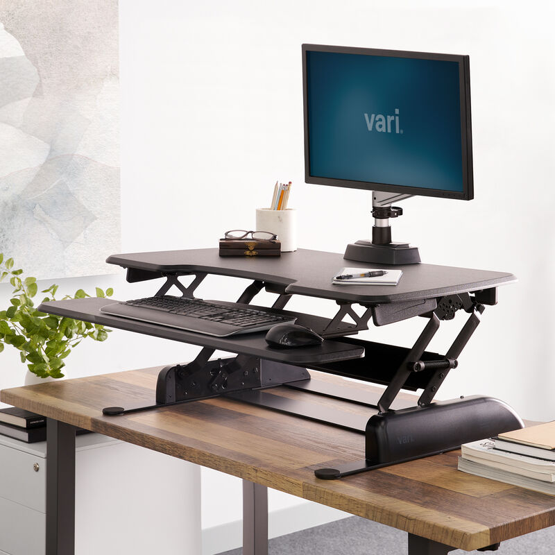VariDesk Essential 36 black converter raised on a host desk with single monitor for context