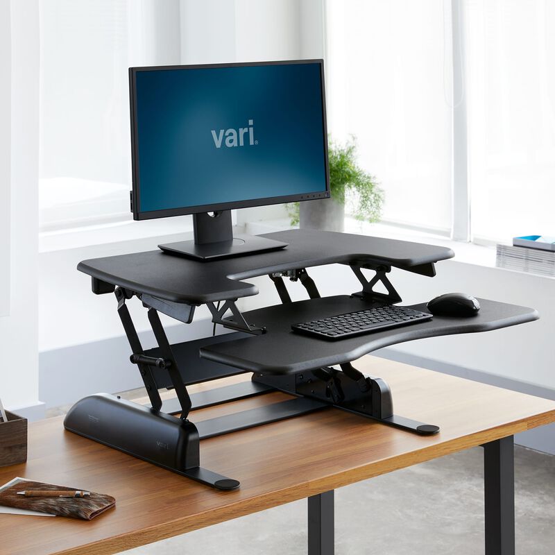 VariDesk Pro Plus 30 black converter raised on a separate host desk; pictured monitor and desk are context