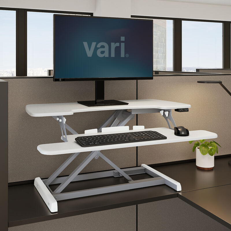 White VariDesk Pro Plus 36 Electric converter raised on a separate host desk; the monitor and arm are scene context.