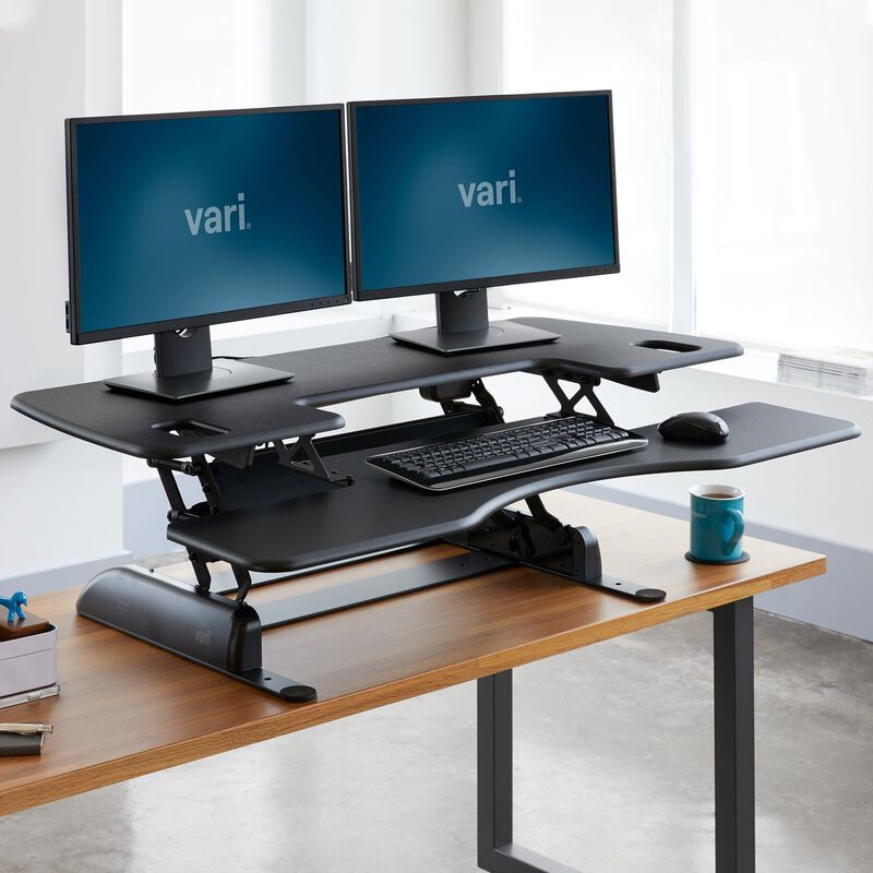 VariDesk Pro Plus 48 black converter raised on a host desk with two monitors; pictured items are contextual