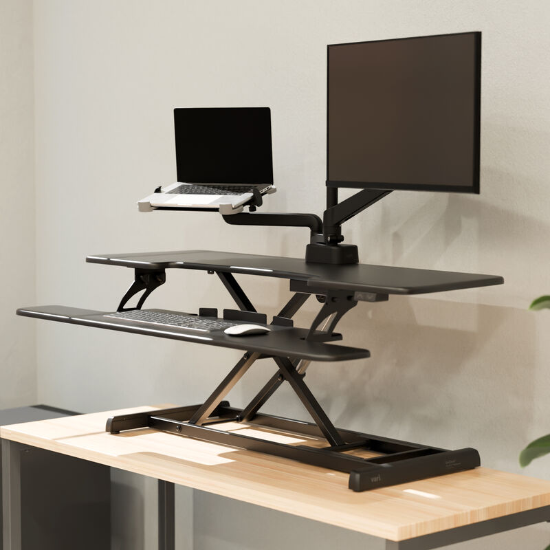 Black VariDesk Pro Plus 48 Electric converter raised on a host desk; display hardware is scene context